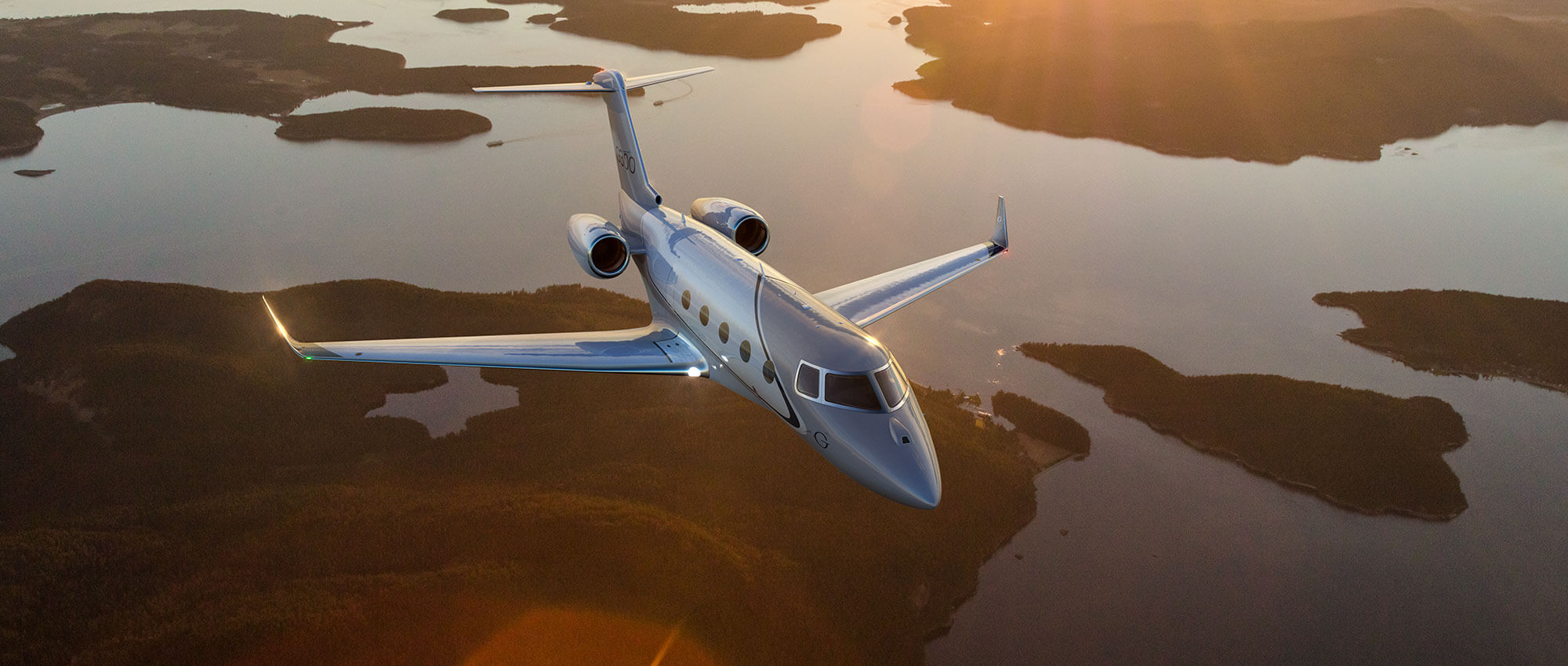 A Gulfstream G300 flies over an island-studded waterway light by a rising sun.