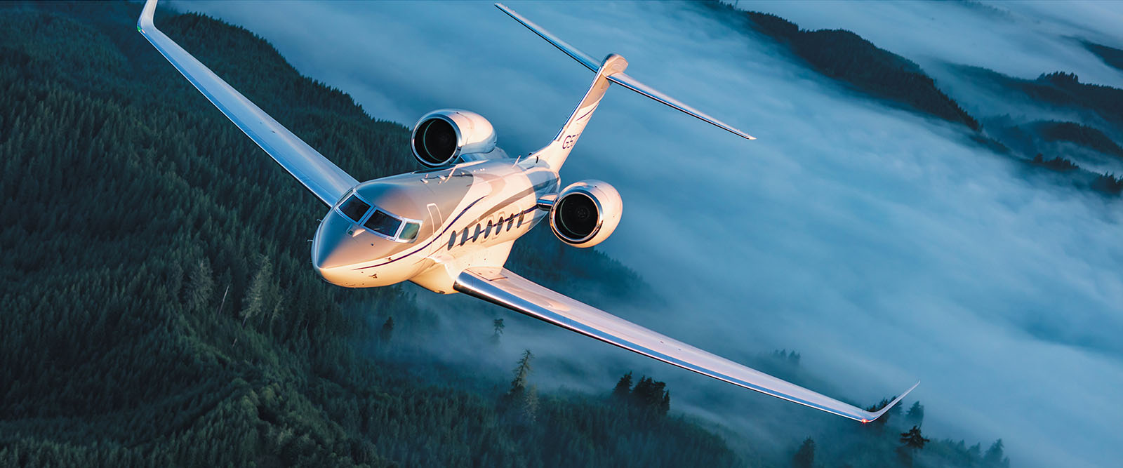 A G500 in morning light flies over a misty, forested landscape