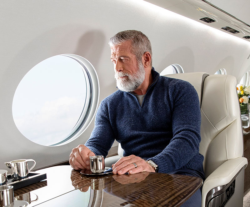 A distinguished, bearded man enjoys a beverage as he gazes out of a panoramic window in a G700