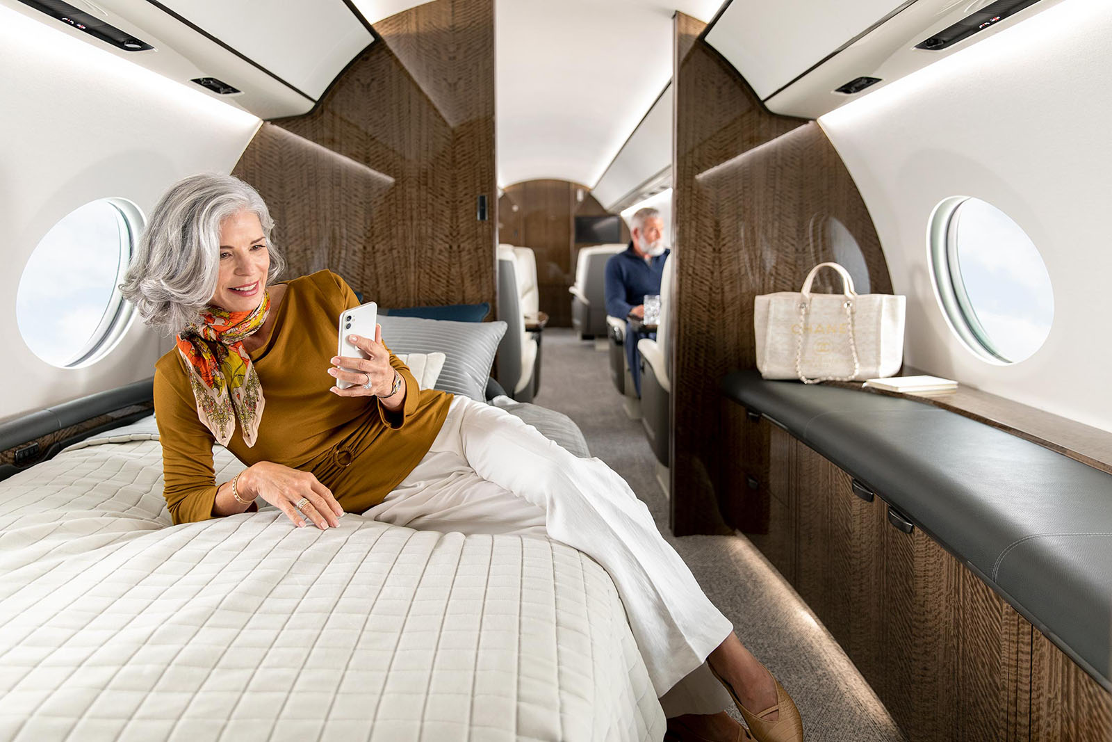 A woman views her smartphone while lounging on the bed of a Gulfstream G700