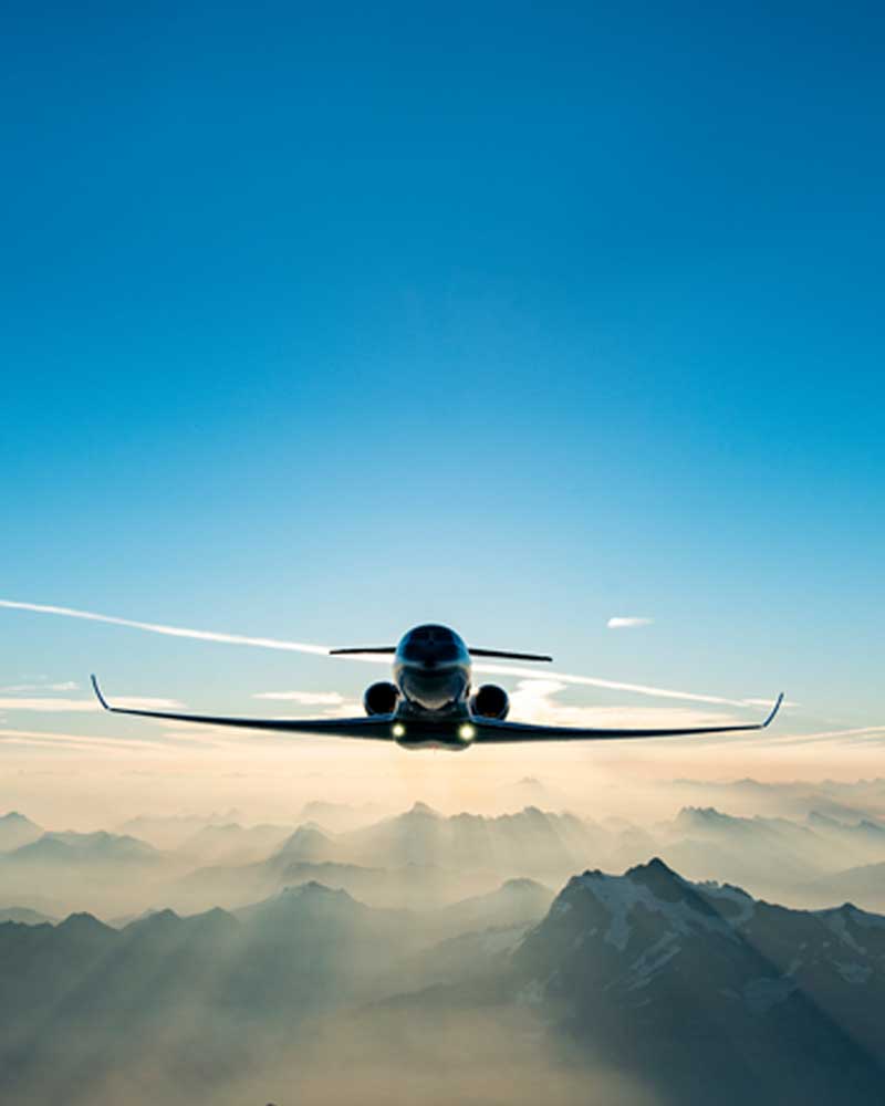 A Gulfstream private aircraft flying toward viewer above misty mountain peaks and backlit by morning sun