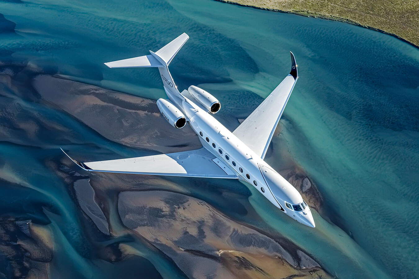 A Gulfstream G700 flies above sparkling blue water cutting channels through sandy green and brown flats