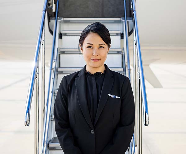 A smiling Gulfstream flight attendant awaits passengers at the bottom of a Gulfstream aircraft entry stair.
