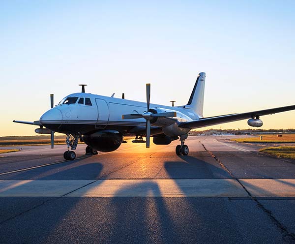 A Gulfstream I stands at one-quarter view on a tarmac, lit from behind by a warm sunrise.