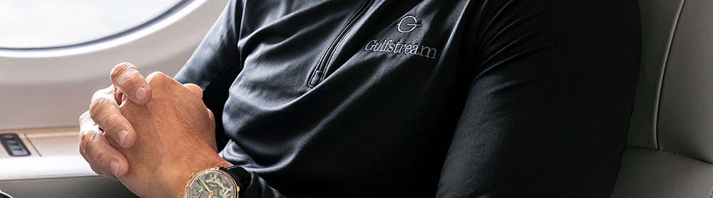 A close-up of a male passenger reclining in a Gulfstream aircraft seat wearing a polo shirt with a Gulfstream logo