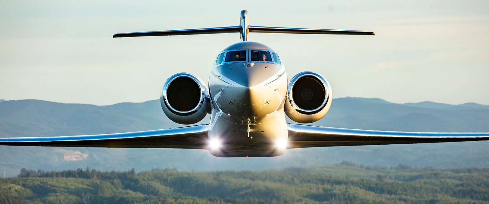 Front view of a Gulfstream G600 flying low to the ground with mountains in the background